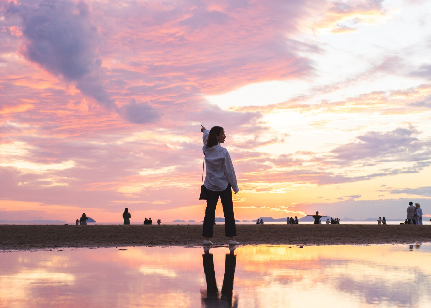 夕焼けの空を指さしている女性