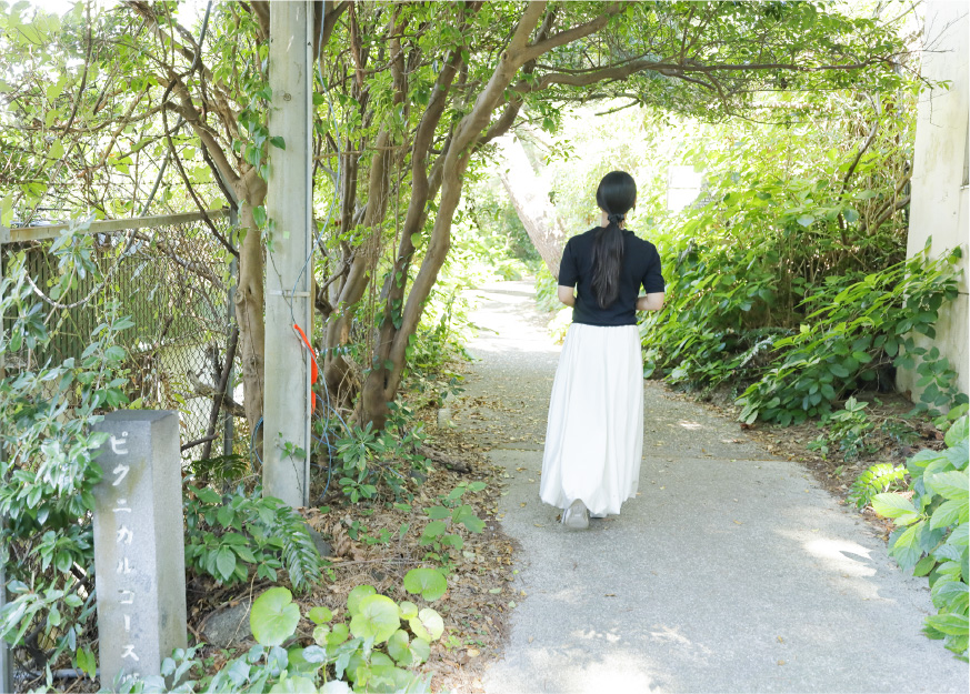 草木に囲まれた小道を歩く女性